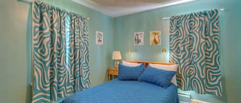 Quarto com cama, cortinas, mesa de cabeceira, abajur e quadros na parede.