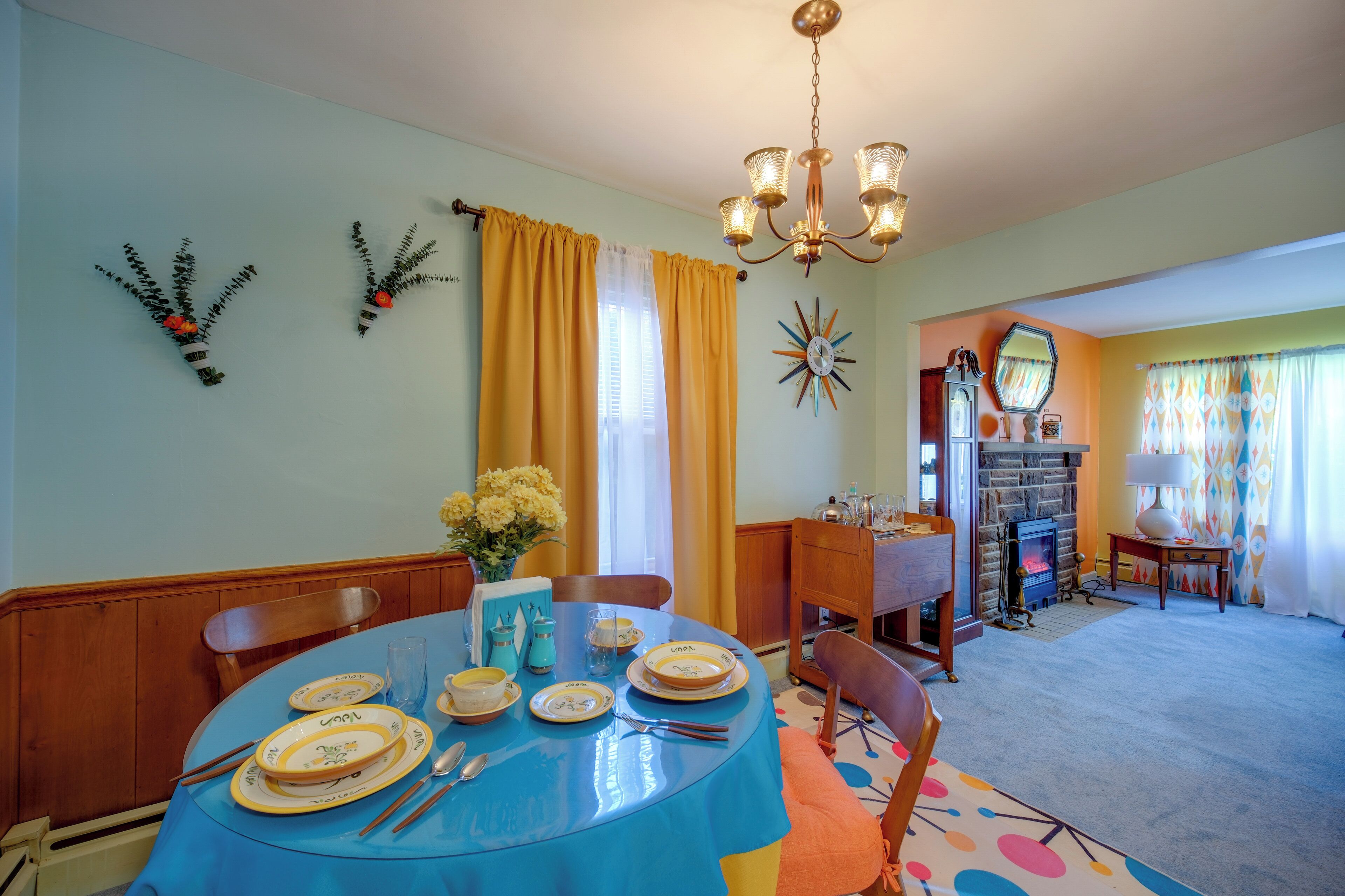 A dining room with a round table set for four, a chandelier, and a fireplace in the background.