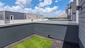 En takterrass med ett platt tak, en liten gräsyta och utsikt över stadens silhuett.