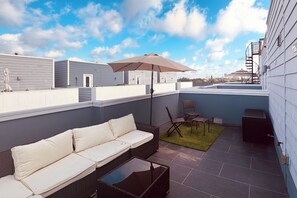 Een terras op het dak met een bank, stoelen, een parasol en een kleine tafel.