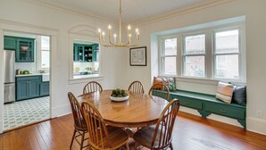 Ein Esszimmer mit Holztisch und Stühlen, einer Chandelierleuchtre und Blick ins Freie durch große Fenster.