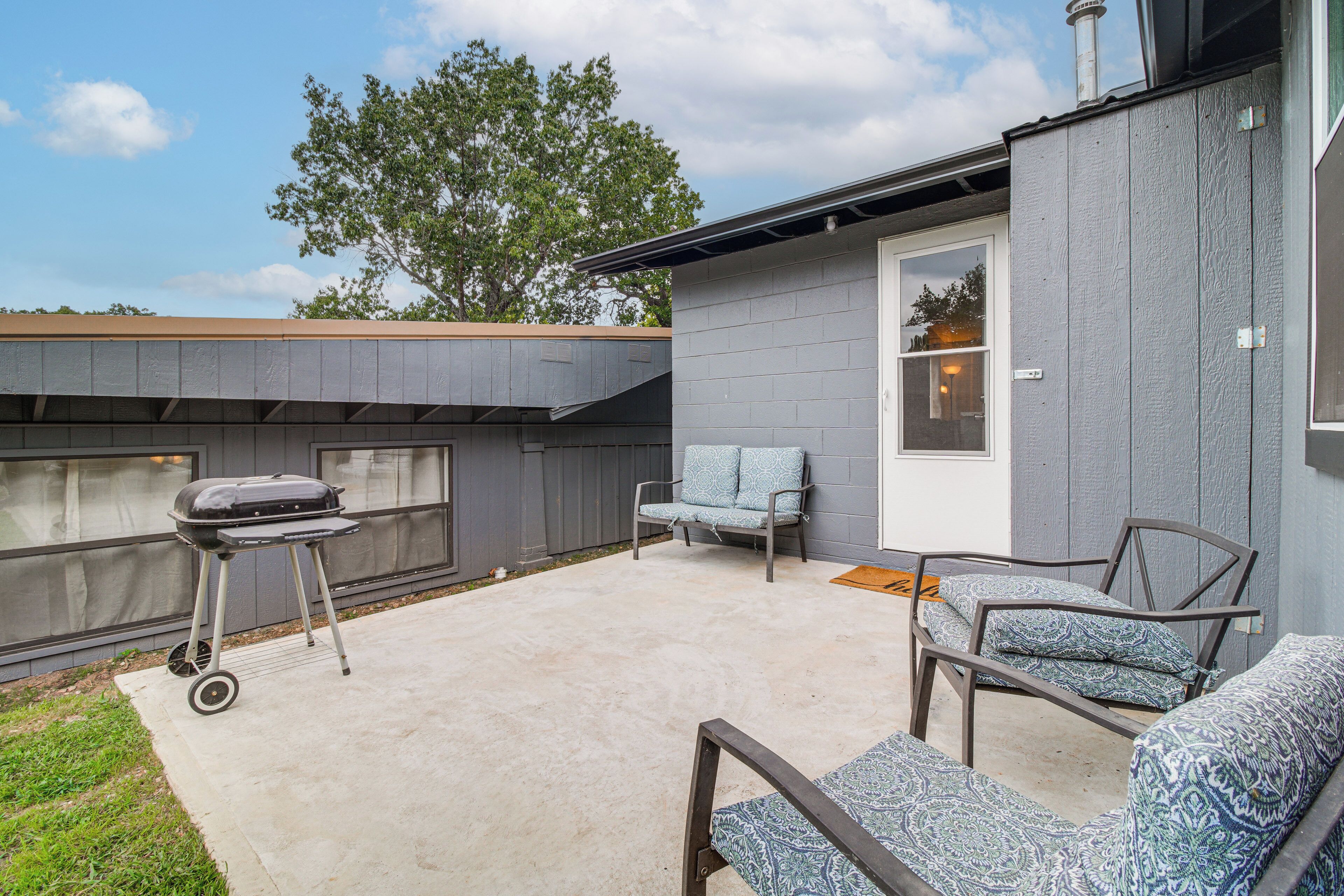 Une terrasse avec un barbecue, des sièges d’extérieur et une porte donnant sur un espace abrité.