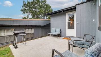 A patio with a grill, outdoor seating, and a door leading to a covered area.
