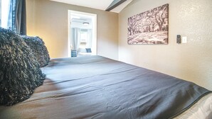 Quarto com cama, porta para banheiro, ventilador de teto e um quadro na parede.