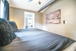 A bedroom with a bed, a door leading to a bathroom, a ceiling fan, and a painting on the wall.