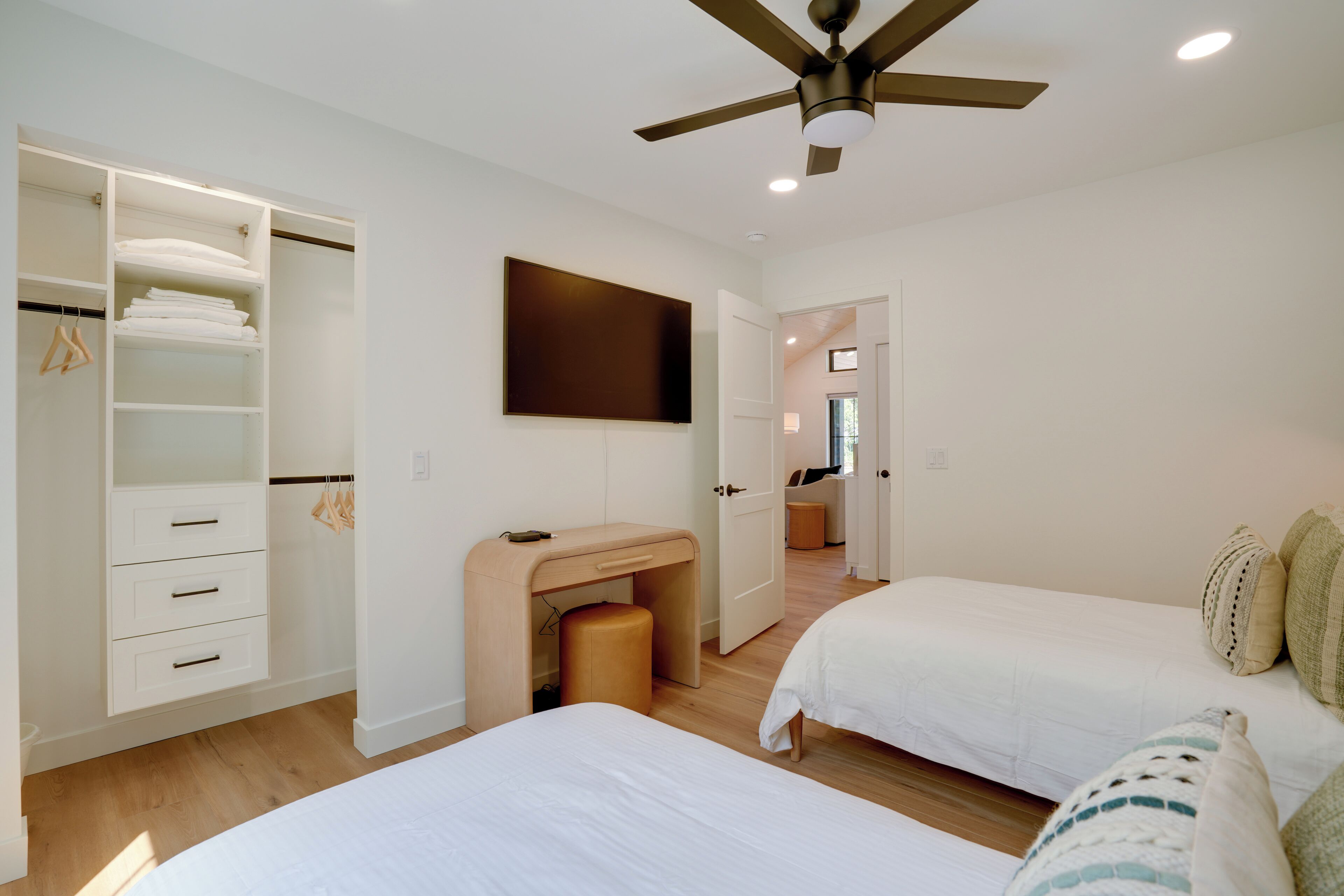 A bedroom with two beds, a wardrobe, a desk, and a ceiling fan.