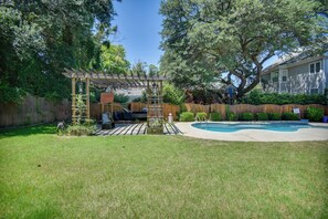 Ein Garten mit einer Holz-Pergola, einem Swimmingpool und einem eingezäunten Bereich.