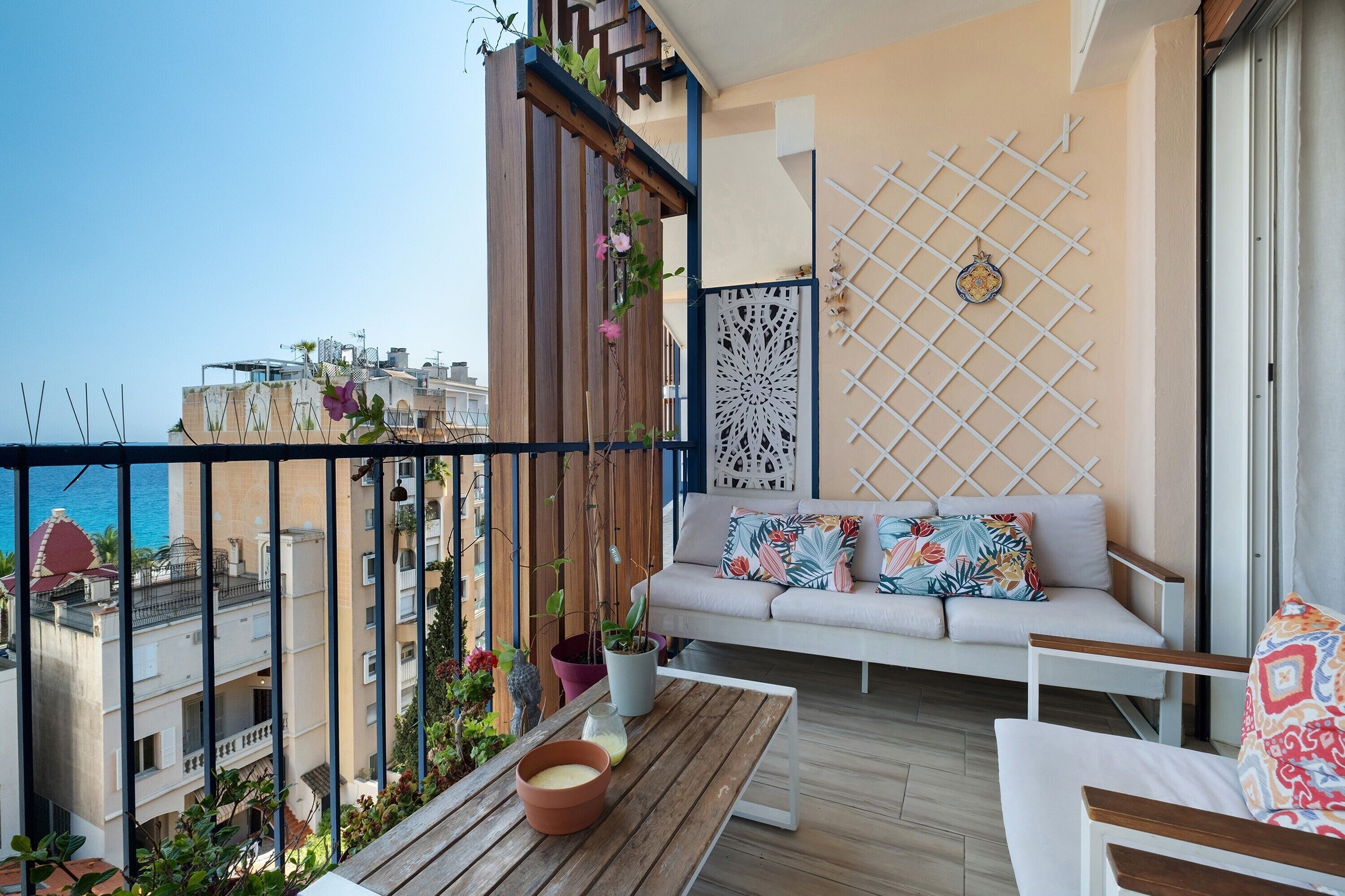 A balcony with a sofa, a wooden table, and potted plants.