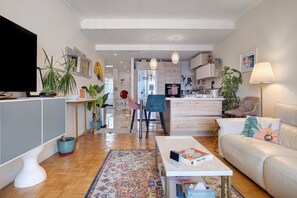 A modern living room with a flat-screen TV, a sofa, a coffee table, and a kitchen in the background. - Sea View 2 Bed & 2 Bath - Highly Rated, with Wi-Fi and Air Conditioning (Nice)