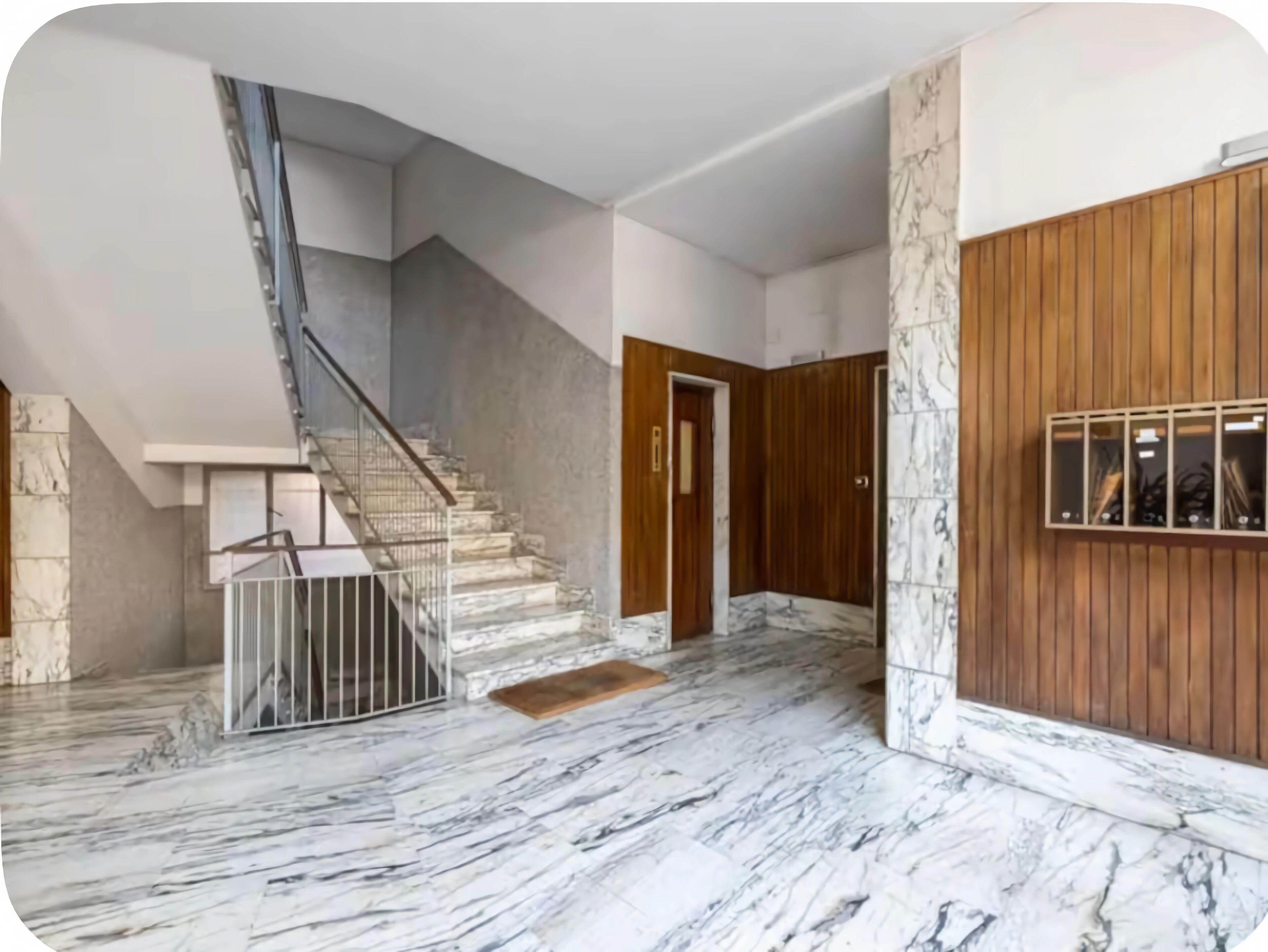 Um interior espaçoso com piso de mármore, uma escadaria e painéis de madeira nas paredes.