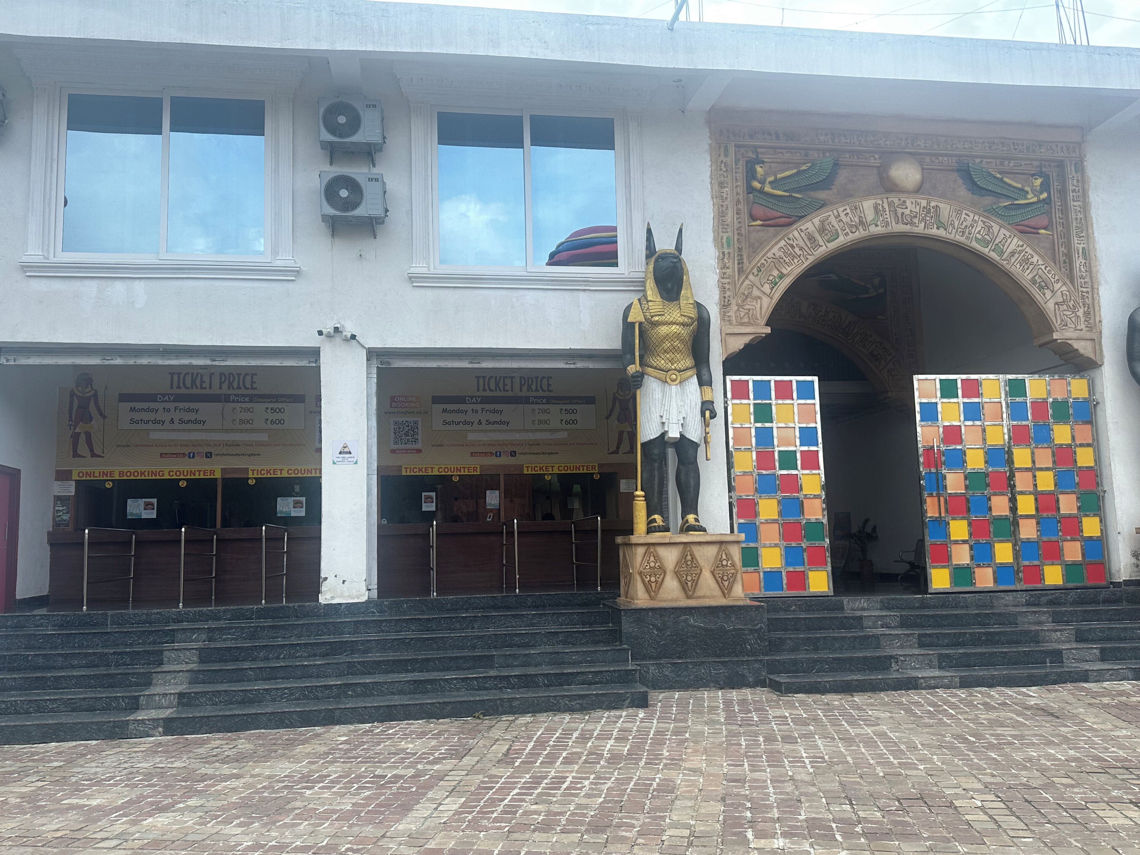 Entrada de un edificio con mostradores de boletos, una estatua egipcia y un mosaico colorido.