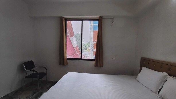 A room with a bed, a chair, and a window with curtains. - Rimjhim Water Kingdom & Resort (Mandar)