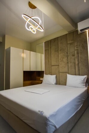 Una habitación de hotel moderna con una cama grande, un cabecero con diseño texturizado y una lámpara colgante.