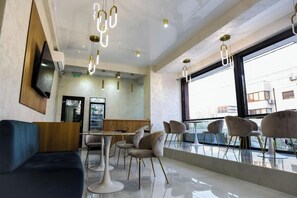A modern interior with a dining area, seating, and a large window. - Beach Vibe Hotel  (Mamaia-Sat)