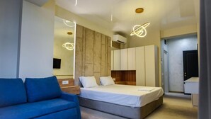 A modern bedroom with a bed, a blue sofa, and a wooden headboard. - Beach Vibe Hotel  (Mamaia-Sat)