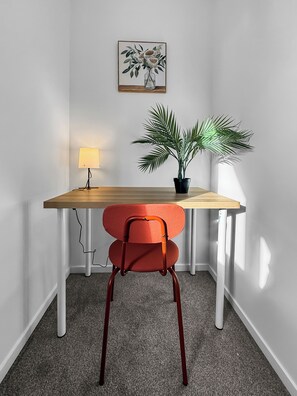 Ett hörnrum med ett skrivbord, en stol, en lampa och en krukväxt.