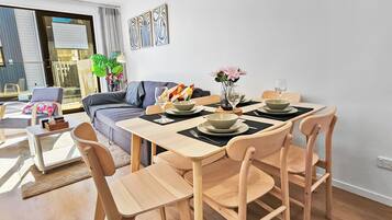 A modern dining area with a wooden table and chairs, a sofa, and a large window with blinds.