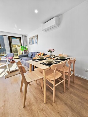 Un comedor moderno con una mesa y sillas de madera, un sofá y un amplio ventanal con persianas.