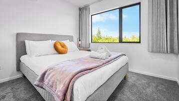 A modern hotel room with a large bed, a window with a view, and a bedside table with a lamp.
