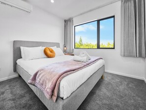 Une chambre d’hôtel moderne avec un grand lit, une fenêtre donnant sur un beau paysage et une table de chevet avec une lampe.