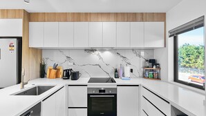 A modern kitchen with white cabinets, a marble backsplash, and a Bosch dishwasher. - Waipuna Living | 3-Bed Townhouse | Spacious Home (Mount Wellington)