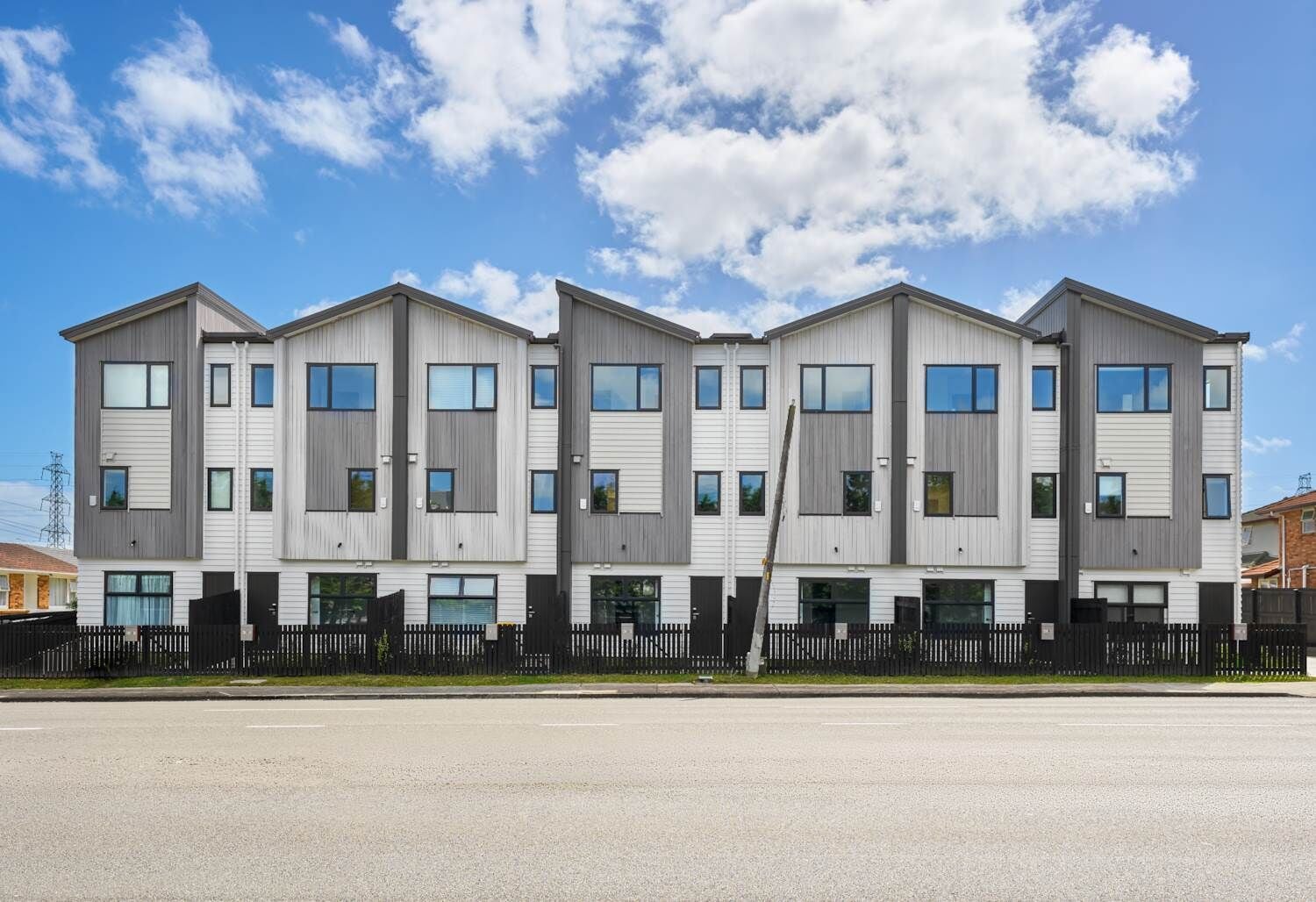 A modern multi-story residential building with a symmetrical facade, large windows, and a black fence in front.