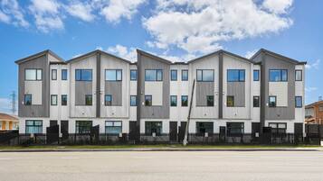 A modern multi-story residential building with a symmetrical facade, large windows, and a black fence in front.