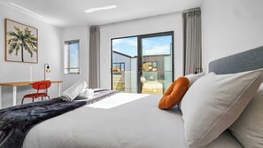 Une chambre d’hôtel moderne, dotée d’un grand lit, d’un bureau, d’une chaise et offrant une vue sur l’extérieur grâce à une porte-fenêtre coulissante.