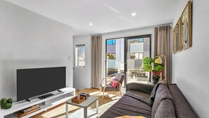 A modern living room with a flat-screen TV, a sofa, a coffee table, and a chair. - Waipuna Living | 3-Bed Townhouse | Spacious Home (Mount Wellington)