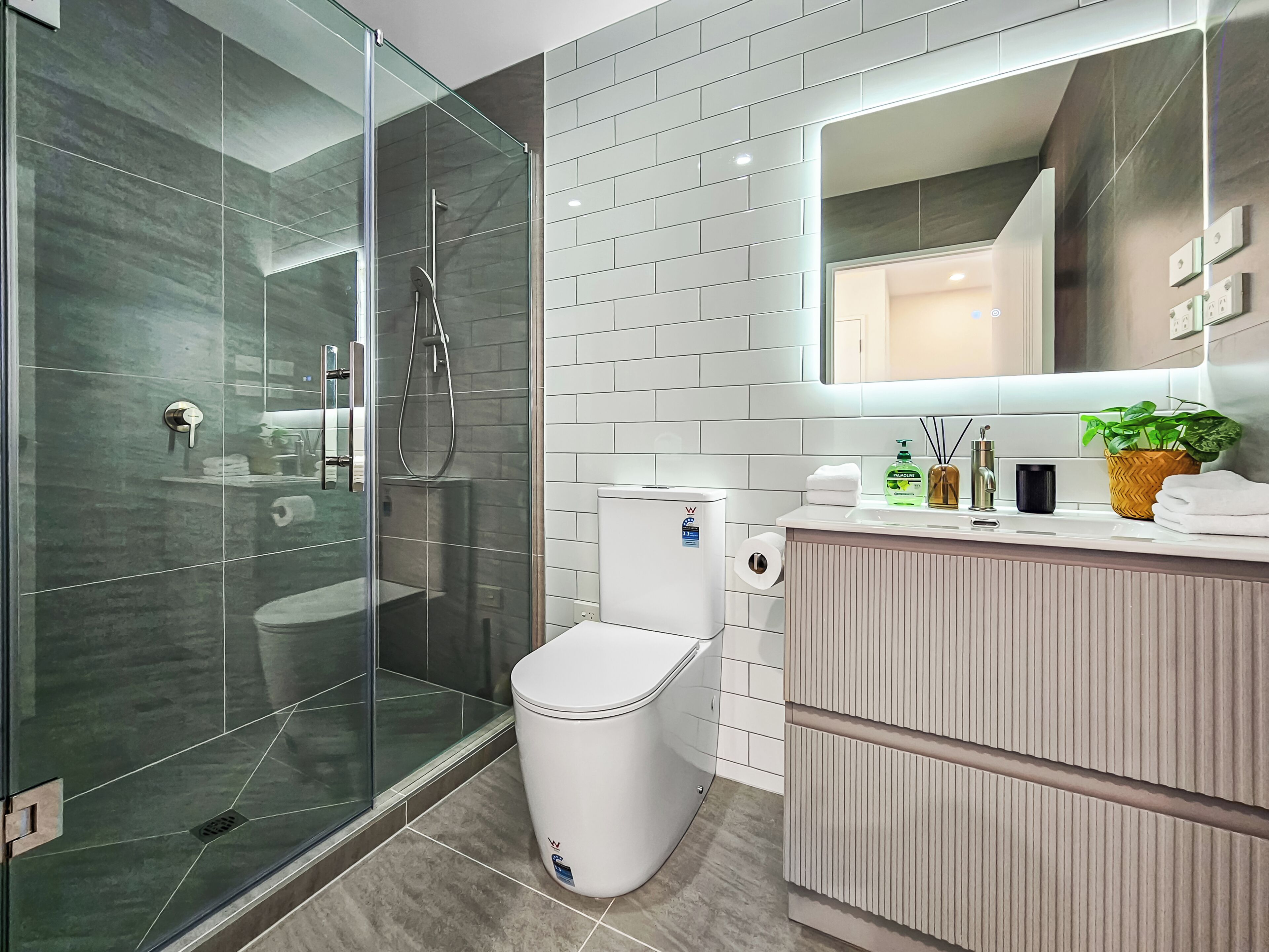 A modern bathroom with a glass-enclosed shower, a toilet, and a vanity with a mirror.