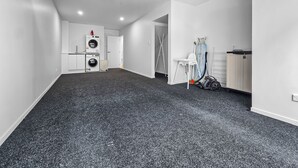 Ett rymligt rum med ett mörkt golv, ett tak med synliga ventilationskanaler, en vit dörr och en tvättstuga med tillhörande utrustning.