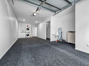 Ein geräumiges Zimmer mit dunklem Teppich, einer Decke mit freiliegenden Lüftungsrohren, einer weißen Tür und einem Waschbereich mit Geräten.