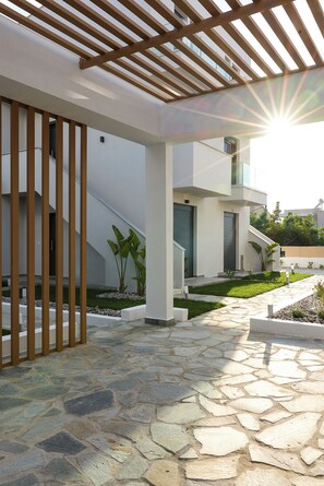 Ein modernes Gebäude mit einem pflasterbelagten Eingang, einer hölzernen Pergola und einem gepflegten Garten.