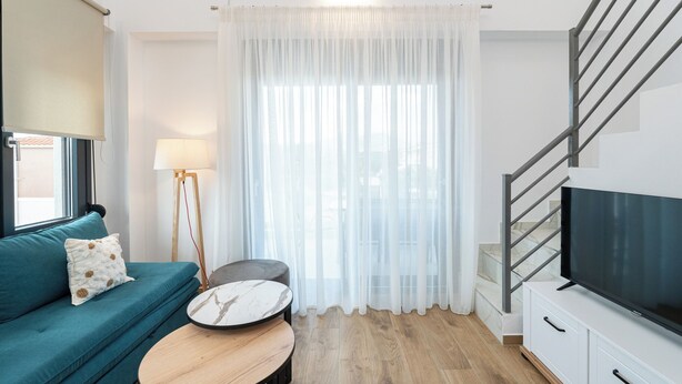 En moderne stue med sofa, sofabord, lampe, fjernsyn og trappe.