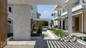 Et overdækket udendørsområde med flisebelagte gulve, en træpergola og moderne bygninger i baggrunden.
