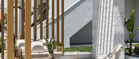 An outdoor seating area with a pergola, stone flooring, and a white wall with a geometric design.