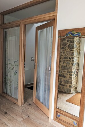 A room with a wooden floor, a sliding glass door, a stone wall, and a mirror with a decorative frame. - Gîte 2 "Le Bateau Yves" by Interhome (Blainville-sur-Mer)