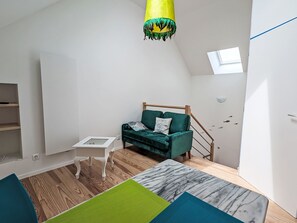Ein modernes Schlafzimmer im Loft-Stil mit einem grünen Sofa, einem kleinen weißen Beistelltisch, einem Bett mit Marmoroptik und Holzboden.