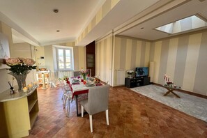 A spacious dining area with a high ceiling and a large window, a living room with a television and seating, and a kitchen area with a window and counter. - A Bright and Cozy Apartment with Stunning Views in the Heart of Lucca (Lucca)