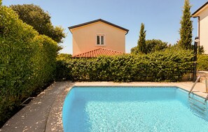A swimming pool with a tiled deck, surrounded by dense greenery and a building with a red-tiled roof in the background. - Stunning home in Porec (Porec)
