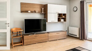 A modern living room with a flat-screen TV, wooden furniture, a white cabinet, and a clock on the wall. - Stunning home in Porec (Porec)
