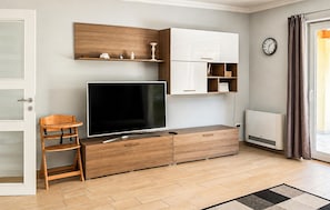 Ein modernes Wohnzimmer mit Flachbildfernseher, Holzmöbeln, einer weißen Kommode und einer Wanduhr.