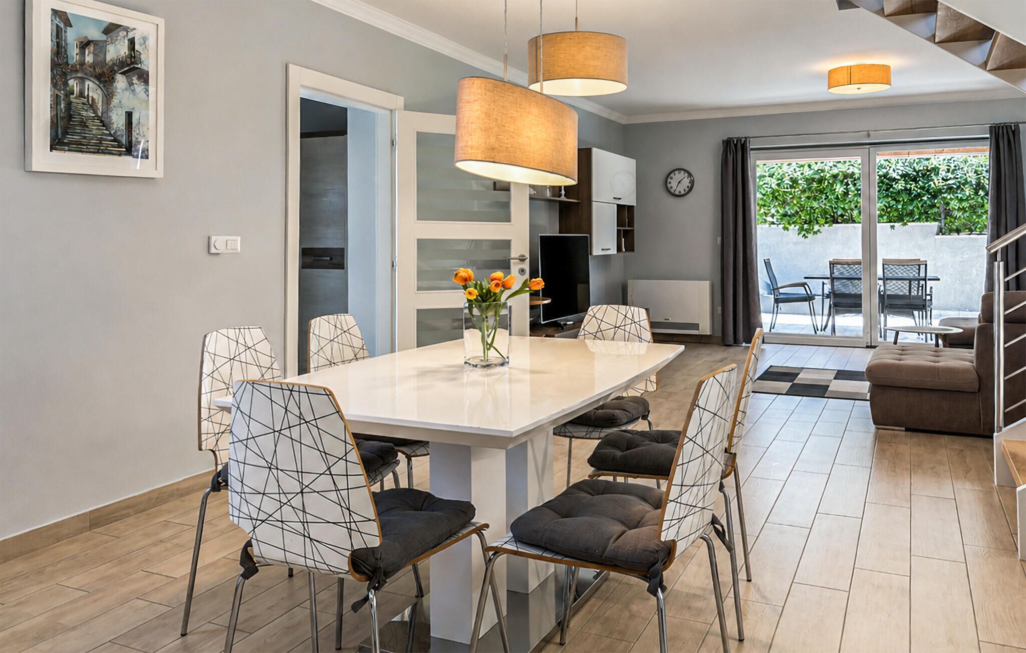 Un espace repas moderne avec une table blanche, des chaises à motifs géométriques et un vase rempli de fleurs.