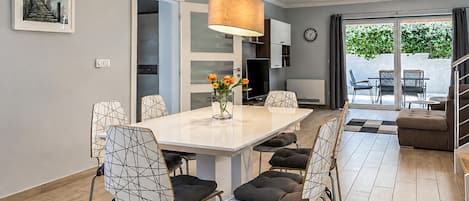 Un espace repas moderne avec une table blanche, des chaises à motifs géométriques et un vase rempli de fleurs.
