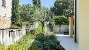 A courtyard with a stone wall, a tree, and a tiled patio area. - Stunning home in Porec (Porec)