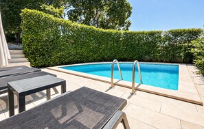 Ein Swimmingpool mit Metallleiter, umgeben von einer Fliesenplattform und einer Reihe dunkler Liegestühle.