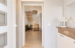 A hallway leading to a staircase with a wooden finish, a white door on the left, and a wooden cabinet with a white lantern on the right. - Stunning home in Porec (Porec)