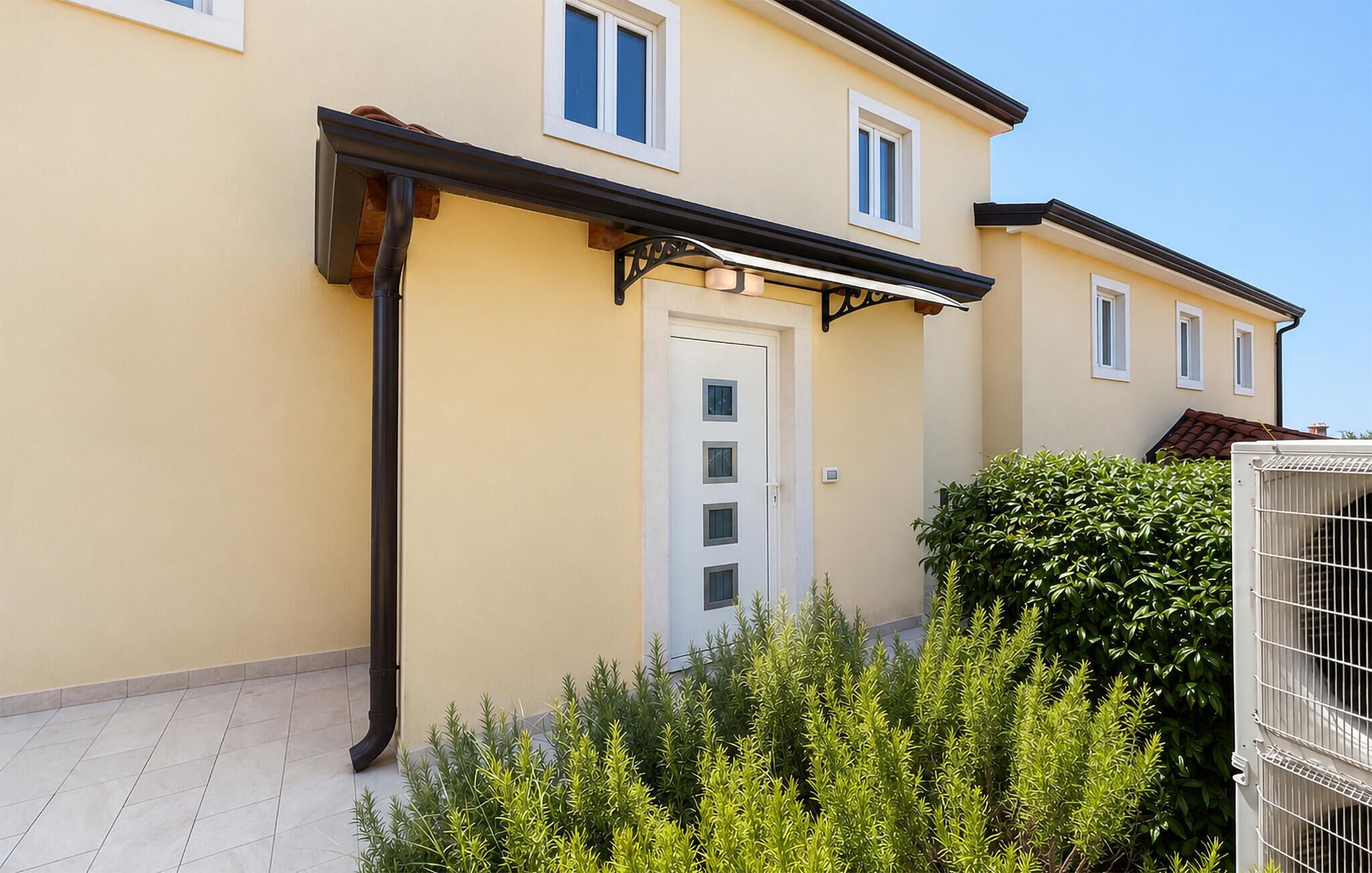 Un immeuble résidentiel doté d’un patio carrelé, d’une porte blanche et d’un système de gouttières noir.