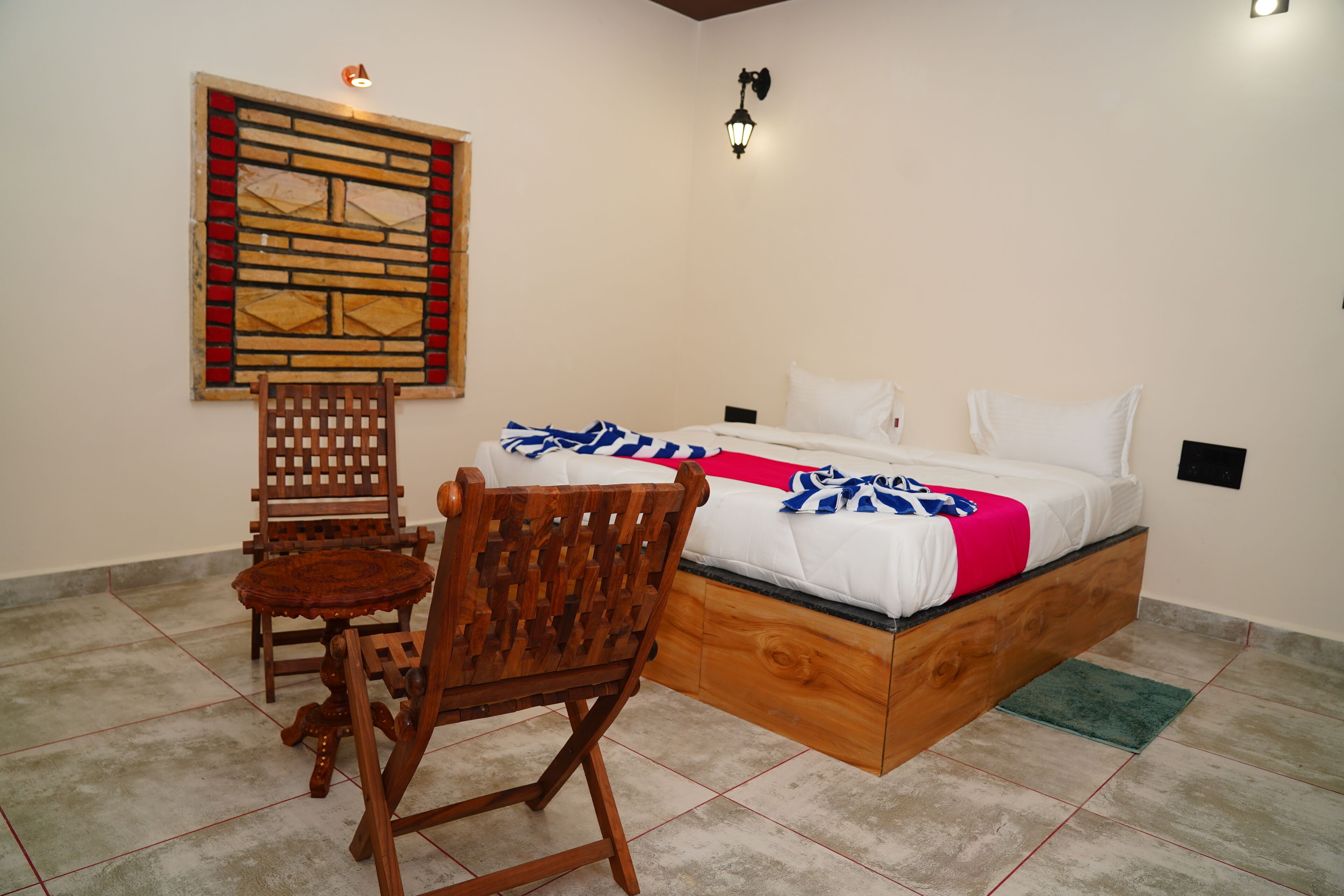Un dormitorio con cama, una silla de madera, una mesita, una lámpara de pared y un adorno en la pared.