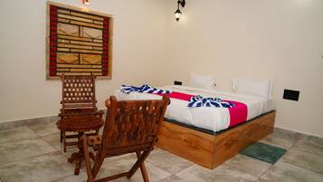 Un dormitorio con cama, una silla de madera, una mesita, una lámpara de pared y un adorno en la pared.